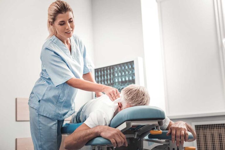 A therapist guides an adult through a strengthening exercise beside a treatment table.